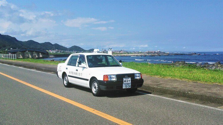 海のそばを走る千倉自動車教習所の教習車
