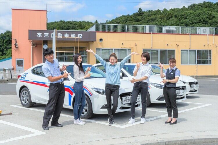 本宮自動車学校の校舎前の教習車と職員